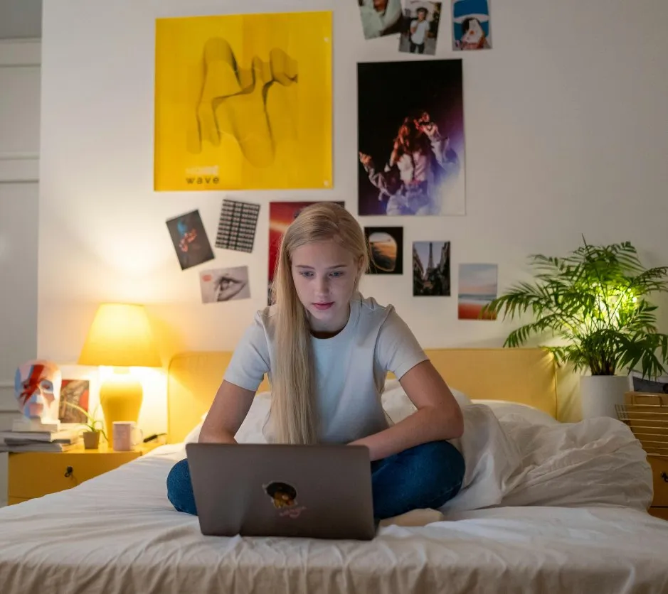 Étudiante assise sur son lit, travaillant sur son ordinateur
